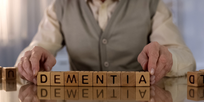 An elderly man holding wooden blocks that spell Dementia 