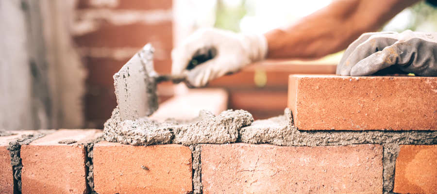 Bricklayer laying cement down on top of a red brick wall