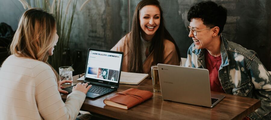 A group of employees sat in a cafe with their laptops laughing